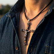 Silver and wood crucifix pendant necklace with detailed corpus on braided leather cord worn by man in denim jacket, showing religious jewelry lifestyle shot in natural lighting