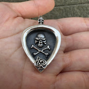 A solid sterling silver skull guitar pick holder pendant, shown being held in a hand to demonstrate its size.