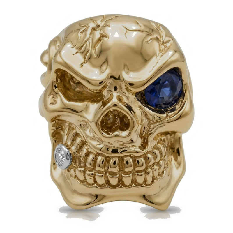 Anello teschio in oro giallo 14K visto di fronte, con occhio di zaffiro blu intenso e dente con diamante.