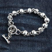 A solid sterling silver bracelet made of small skull links, shown on a blue jeans background.