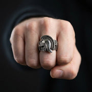 Anello con elmo romano spartano in argento con intricate incisioni tribali indossato sul dito medio di un uomo, esposto su un pugno chiuso contro uno sfondo nero scuro