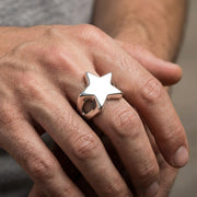 Close-up of a male model's hand wearing a large silver star ring with a 25mm face size, captured in soft editorial studio lighting.