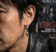 Close-up of a rocker model wearing a sterling silver dangle skull hoop earring, showcasing drop design in soft studio lighting.