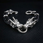 Sterling silver dual dragon head bracelet with black braided leather band and dragon claw clasp on black leather background