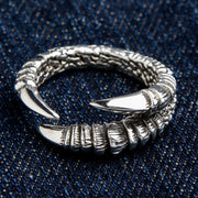 A solid sterling silver eagle claw ring in a powerful wrap-around design, shown on a dark denim background.