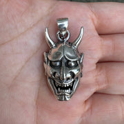 A solid sterling silver Hannya mask pendant held in hand, showing its detailed demonic face.