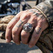 Sterling silver iron cross ring with red garnet stone worn on tattooed hand with motorcycle in background