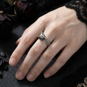 Sterling silver adjustable owl ring with detailed feather and eye design worn on a woman's ring finger against a dark gothic background with black lace and dried roses