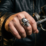 Close-up of a sterling silver punk skull ring worn on a hand holding a chopper accelerator, set against dark leather clothing for a moody biker lifestyle look.