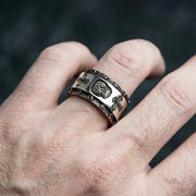 Close-up of a male hand wearing a wide sterling silver Santa Muerte ring featuring a central skull motif, flanking crosses, and small red gemstone accents along the textured borders.