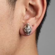 Close-up of a model wearing a detailed sterling silver Tibetan Devil Mask stud earring featuring a fierce expression, three eyes, and a small gold skull accent on top.