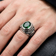 A close-up of a male hand wearing a tiger dragon ring with a green stone, showcasing under soft studio lighting.