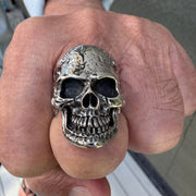 A man's hand wearing the large tough head skull ring, showcasing its rugged, battle-worn texture.