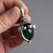 Vue rapprochée d'une main tenant un pendentif gothique détaillé en argent sterling avec grande pierre de lune vert profond sertie dans un design griffes tribales sur fond gris neutre.