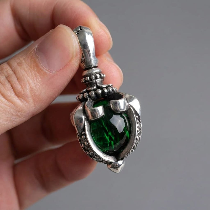 Vue rapprochée d'une main tenant un pendentif gothique détaillé en argent sterling avec grande pierre de lune vert profond sertie dans un design griffes tribales sur fond gris neutre.