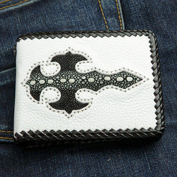 La billetera de biker de cuero blanco hecha a mano con una incrustación de cruz gótica de rayas negras, descansando sobre unos jeans azules.