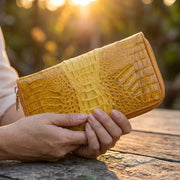 Person holding yellow genuine crocodile leather wallet outdoors at sunset