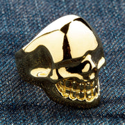 A large yellow gold skull ring with a brilliant 14k gold plating and a flawless high-polish finish, shown on a denim background.