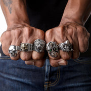 Front view of the sterling silver baroque skull ring with green emerald eyes and gold-plated teeth on finger.
