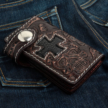 Mørkebrun koskindspung med håndpræget dødningehoved og kors indlagt med sort øgleskind på denim.