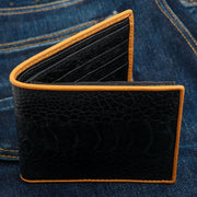 The black genuine ostrich leg wallet with tan trim, sitting on a pair of blue jeans.