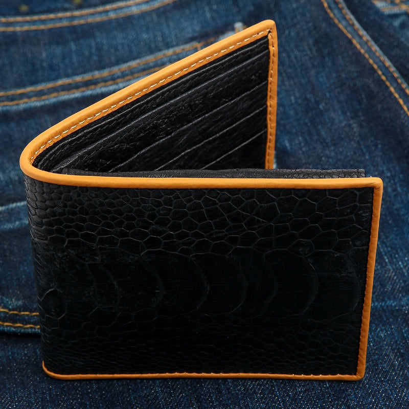 La borsa da polso in pelle di struzzo nero autentico con bordo marrone, posata su un paio di jeans blu.