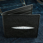 A black genuine stingray leather wallet with its distinctive white pearl mark, shown resting on a denim background.