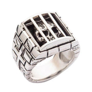A solid sterling silver caged skull ring, featuring a detailed skull behind the bars of a prison cell with a stone wall band.