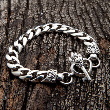 Un pulsera de plata esterlina pesada gótica con cierre de mariposa de corazón y llave, sobre un fondo de madera oscura.