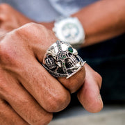 A lifestyle shot of a man wearing the green eye skull ring with a watch in the background.
