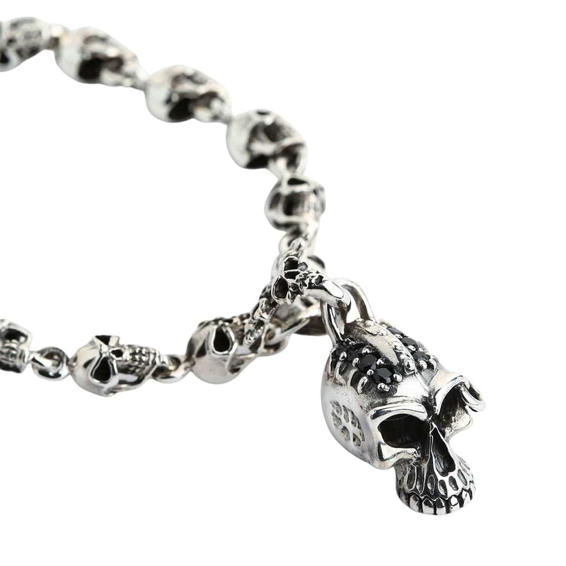 Un sólido brazalete de plata esterlina punk con un collar de cráneos detallados y un charm de cráneo más grande con joyas negras.