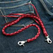 The red braided leather wallet chain with silver-tone clasps, coiled on the back pocket of a pair of blue jeans.