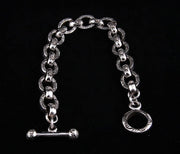 A sterling silver link bracelet with an engraved tribal vine pattern and a T-bar toggle clasp, shown on a black background.