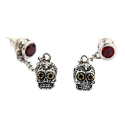 A pair of solid sterling silver dangle sugar skull earrings with brilliant red gemstone studs and golden-eyed Calavera charms.