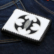 The handmade white leather biker wallet with a black stingray scorpion inlay, resting on blue jeans.