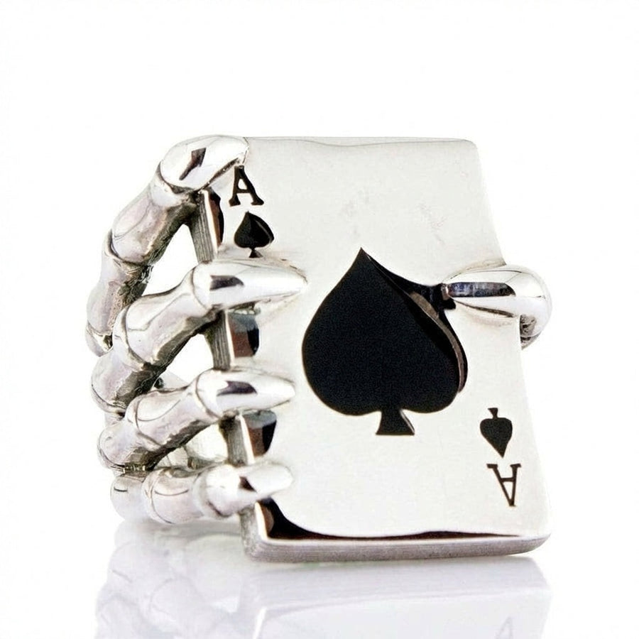 Vista frontale dell'anello Ace of Spades con una mano scheletrica che stringe una carta da gioco con un picche in smalto nero.