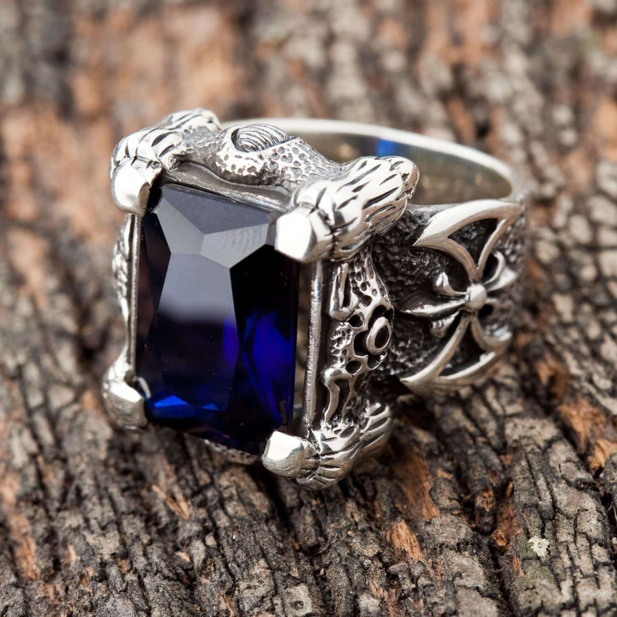Un anello a forma di artiglio di drago in argento sterling che tiene una grande pietra rettangolare smeraldo-blu su uno sfondo bianco.