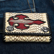 The handmade natural cobra skin biker wallet with a red stingray cross inlay and silver snaps, resting on blue jeans.