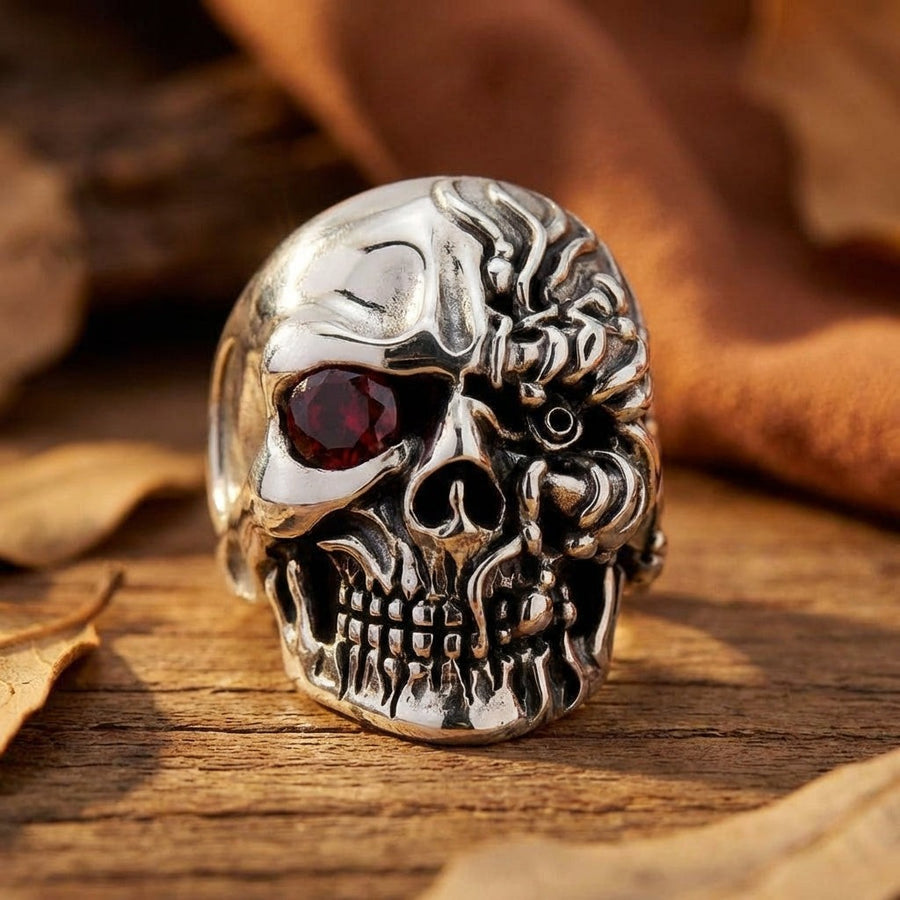 Anillo de calavera Cyborg Terminator en plata de ley con ojo de rubí rojo exhibido sobre una superficie de madera con hojas de otoño