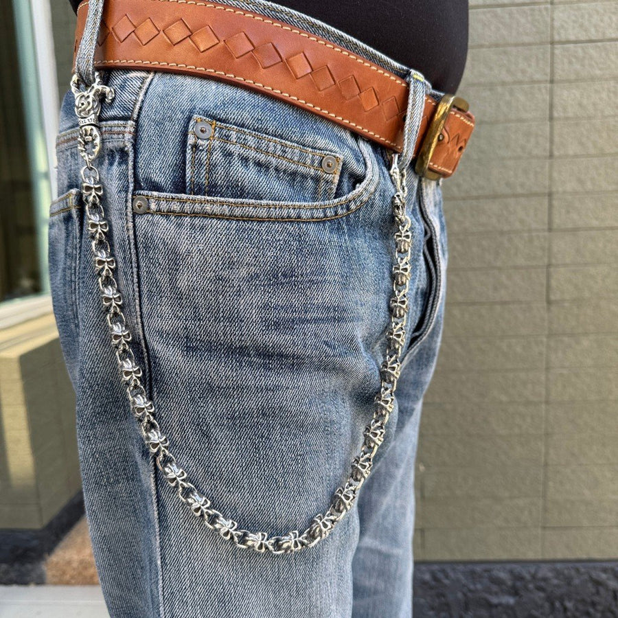 Cadena de cartera de calavera demoníaca en plata de ley 925, pesada, con cierres de llama, sujeta a la trabilla de unos vaqueros azules desgastados con cinturón de cuero marrón.