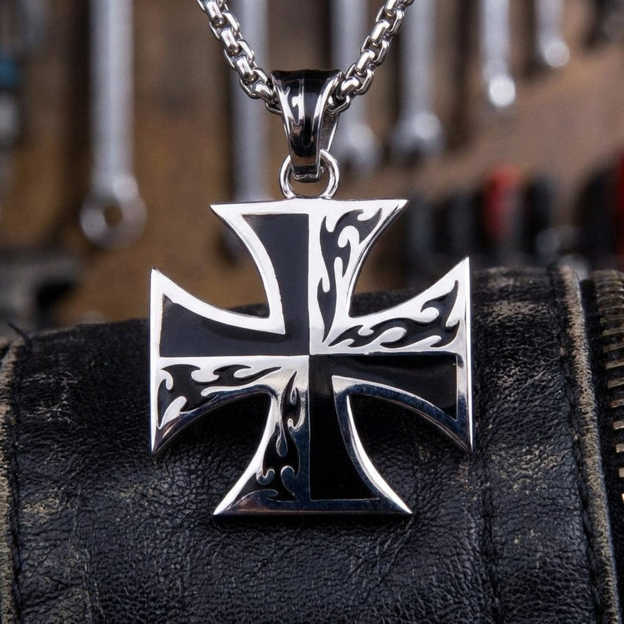 Collana con pendente Iron Cross in argento sterling con motivo a fiamme tribali su smalto nero, su cinturino in pelle nera con attrezzi da officina sullo sfondo.
