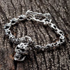 Volledig aanzicht van de 57 g sterling zilveren doodskopschakelarmband op donker hout, met toggle-sluiting van gekruiste botten en hangende doodskopbedel.