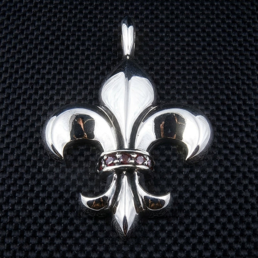 Pendentif en argent sterling en forme de fleur de lis avec des pierres de grenat rouge sur la bande centrale, vue de face sur un fond texturé noir.