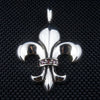Pendentif en argent sterling en forme de fleur de lis avec des pierres de grenat rouge sur la bande centrale, vue de face sur un fond texturé noir.