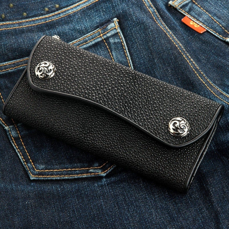 Cartera motera triple de piel de raya negra con cierres de presión de plata con diseño de llamas sobre tejido denim oscuro.