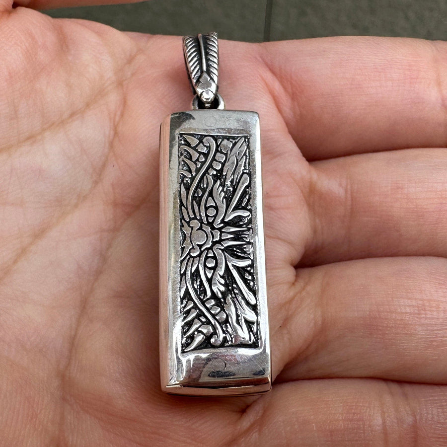 A frente do pendente de mini harmónica japonesa segurado na mão, mostrando a intrincada gravação do rosto de um demónio tribal.