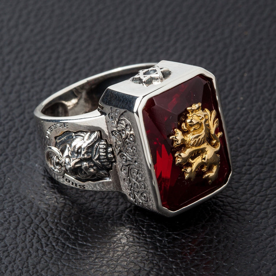 Un anello da uomo in argento massiccio con un emblema di leone rampante in ottone dorato su una grande pietra rossa.