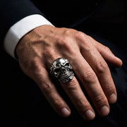Man's hand wearing a large sterling silver skeleton skull ring, showcasing detailed biker jewelry craftsmanship and gothic style fit