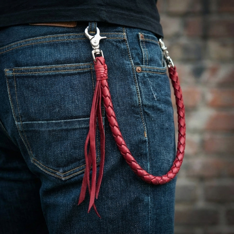 Chaîne portefeuille en cuir tressé rouge bordeaux avec clips en métal argenté attachée à la poche arrière d'un jean bleu avec pompons décoratifs en cuir