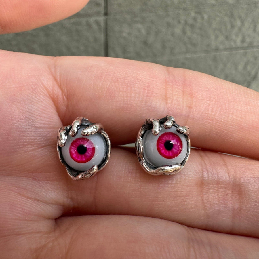 Par de pendientes de botón con ojo de cristal rojo sujeto por garras de plata de ley, sobre una palma abierta.
